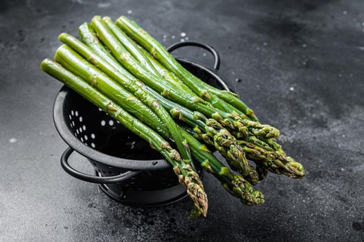 Raw green asparagus in a old colander. Black background. Top view.