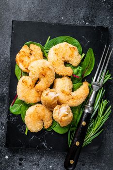 Roasted Crispy Shrimps Prawns on a marble board with green salad. Black background. Top view.