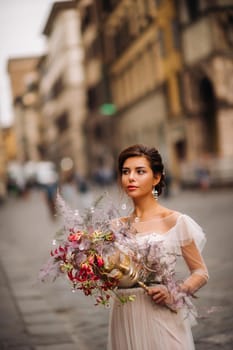 the girl-bride is with beautiful flower pattern as a mask in Florence, stylish bride in a wedding dress standing with a mask in the Old town of Florence. Model girl in Florence.