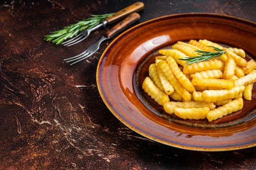 Fried Crinkle French fries potatoes or chips in a rustic plate. Dark background. Top view. Copy space.