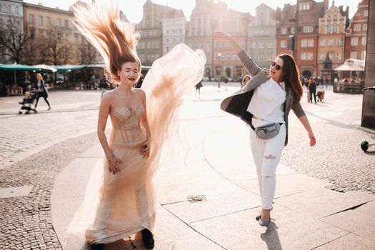 A girl throws a wedding dress to a Bride with long hair in the Old town of Wroclaw. Wedding photo shoot in the center of an ancient city in Poland.Wroclaw, Poland.