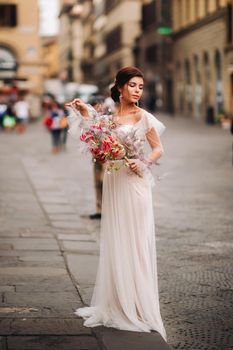 the girl-bride is with beautiful flower pattern as a mask in Florence, stylish bride in a wedding dress standing with a mask in the Old town of Florence. Model girl in Florence.