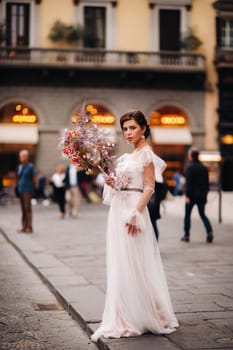 the girl-bride is with beautiful flower pattern as a mask in Florence, stylish bride in a wedding dress standing with a mask in the Old town of Florence. Model girl in Florence.