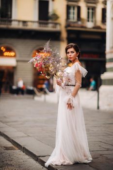 the girl-bride is with beautiful flower pattern as a mask in Florence, stylish bride in a wedding dress standing with a mask in the Old town of Florence. Model girl in Florence.