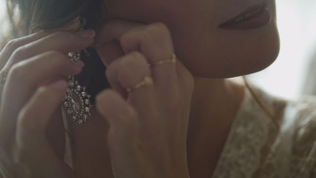 Bridesmaid puts earrings on bride's ear, close up