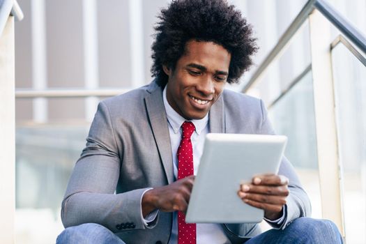 Black Businessman using a digital tablet sitting near an office building. Man with afro hair.