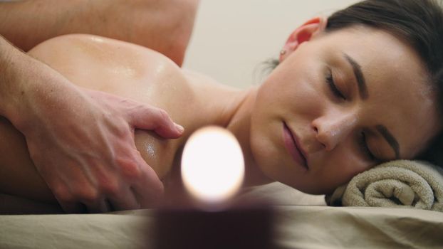 Young female relaxing in spa salon - oil sesame massage table, close up