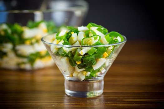 fresh spring salad with boiled squid, boiled eggs and green onions on a wooden table