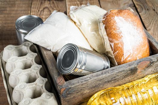 Wooden box with Donation food, quarantine help concept. Oil, canned food, pasta, bread, sugar, egg. Wooden background. Top view.