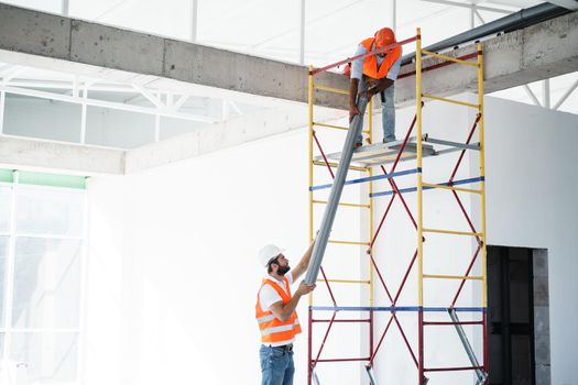 Two men builder in work uniform drag the pipe on scaffolding at construction site