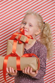 cute cheerful preschooler girl with gifts on a red striped background, gifts with a red ribbon in the hands of a girl with blond hair, boxing day, gifts for birthday and christmas, holiday gifts