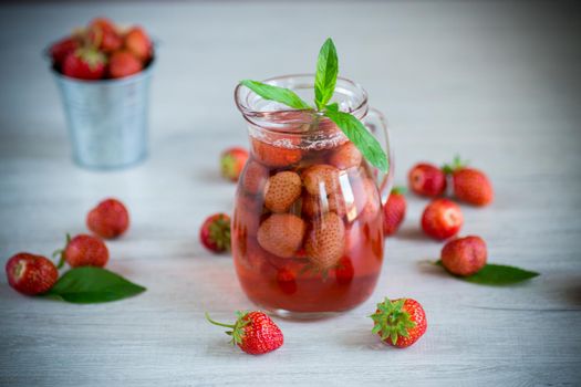 Sweet refreshing berry compote of ripe strawberries in a decanter on a wooden table