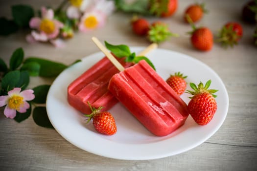 homemade strawberry ice cream on a stick made from fresh strawberries in a plate on a wooden table