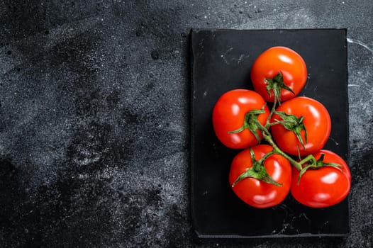 Branch of Red cherry tomatoes on marble board. Black background. Top view. Copy space.