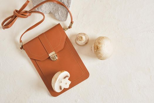 small brown bag for smartphone and credit cards and champignons on a beige background, vegan leather concept, alternative to animal skin, leather from mushroom mycelium