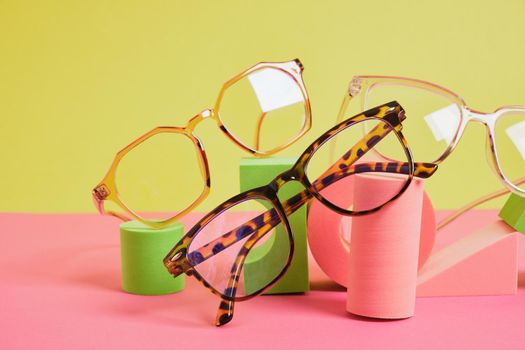 several different trendy eye glasses on geometric pink podiums, colorful background, copy space