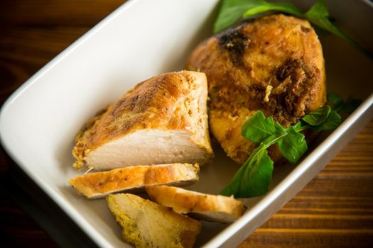 baked chicken fillet pieces with spices and herbs, in a ceramic form on a wooden table