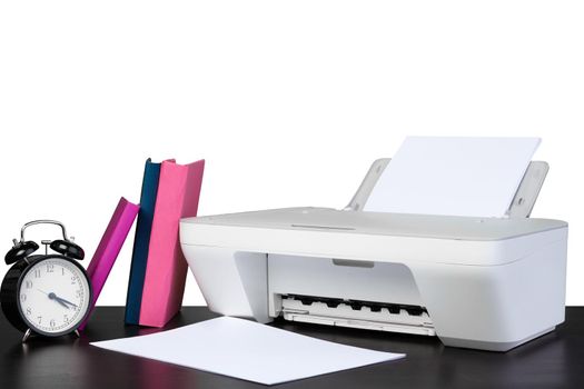 Printer and stack of books on black table against white background, close up