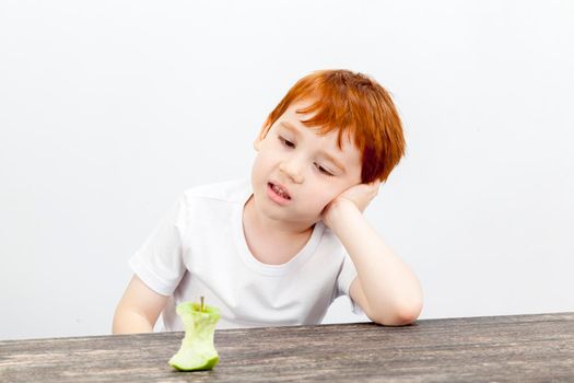 portrait of a boy with red hair and freckles at a kitchen table, looking at a stub of a large apple eaten, little used post-processing a portrait, a boy eating too much apple