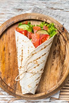 Wrap salmon sandwich, roll with fish and vegetables. White wooden background. Top view.