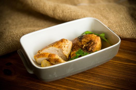 baked chicken fillet pieces with spices and herbs, in a ceramic form on a wooden table