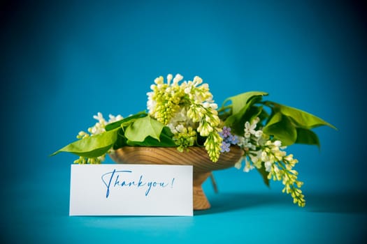 bouquet of white lilacs with greeting card on blue background