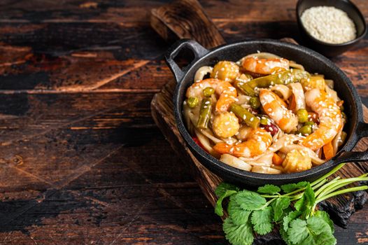 Asian Udon stir-fry noodles with shrimps prawns in a pan. Dark wooden background. Top view. Copy space.