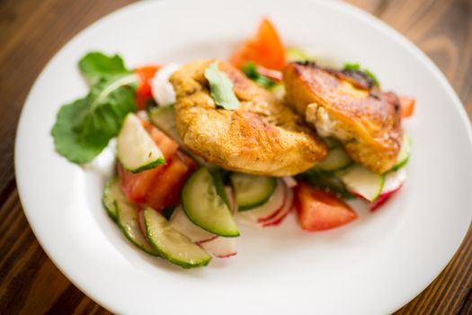 fried chicken fillet with fresh cucumbers, tomatoes and radishes in a plate on a wooden table