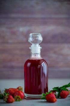 sweet cooked strawberry syrup in a glass decanter on a wooden table