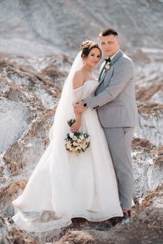 A beautiful couple of lovers posing in a white salt mountain. A young woman in a stylish wedding dress and a beautiful stylish man in a gray suit. The concept of the wedding day