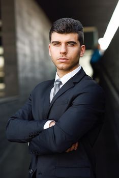 Young businessman near a modern office building wearing black suit and tie. Man with blue eyes