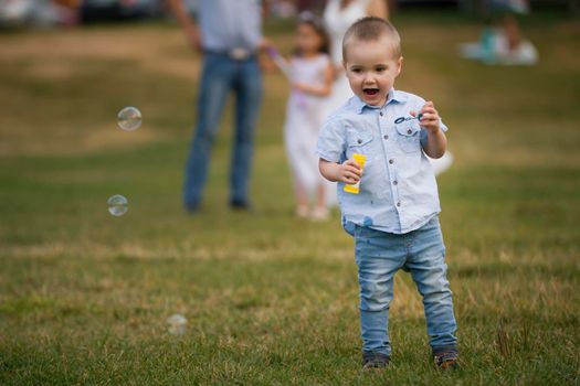 Family during walking in park - little boy blowing soap bubbles, telephoto shot