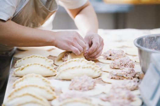 Cook is shaping meat pies by hands in the bakery close-up