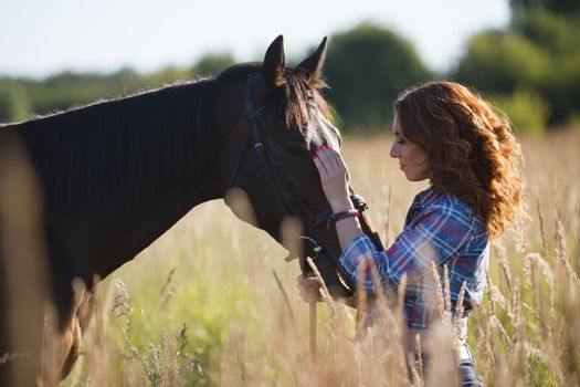 Young woman and horse in the meadow at summer evening, telephoto