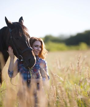 Woman and horse in the meadow at summer evening, telephoto