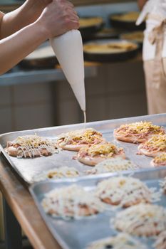 Cook puts the sauce on the mini pizza in the bakery close-up