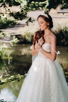 An elegant bride in a white dress, gloves with a bouquet on a waterfall in the Park, enjoying nature.Model in a wedding dress and gloves in the forest.Belarus.
