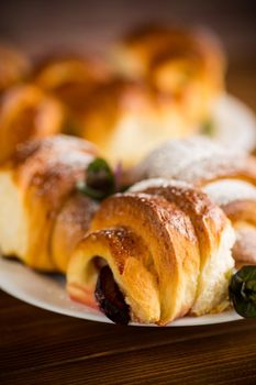 baked sweet homemade buns with plum inside, on a wooden table.