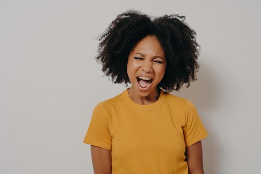 Young beautiful African American woman with curly hair wearing casual yellow tshirt shouting with anger and madness, girl is frustrated and furious. Rage and aggressive concept