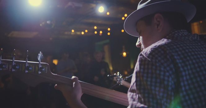 Musician - guitarist in hat plays guitar in night club, rear view, close up