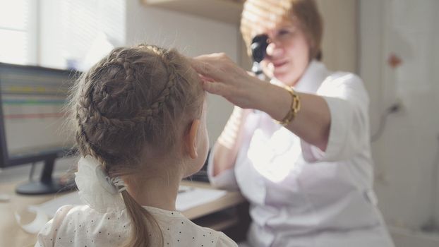 Woman optometrist in clinic checks eyesight at little girl - child's ophthalmology, telephoto