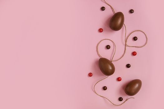 Flat lay composition with chocolate Easter eggs and chocolate sweets on pink background. View from above, empty space for text.