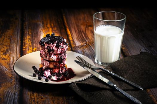 Cheesecakes with blueberry jam and sour cream on a plate with a glass of milk on the table.