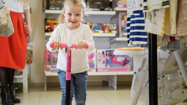 Happy little girl plays with bicycle in kids store, close up