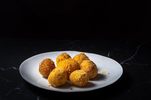 cheese balls with garlic and dill inside for a snack in a white plate on a black background.