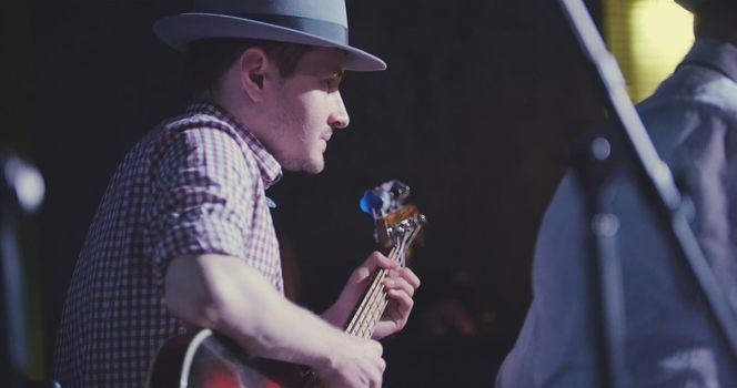 Musician in hat plays guitar in night club, close up, telephoto