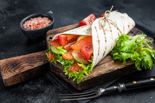 Tortilla Wrap salmon roll with salad, vegetables. Black background. Top view.