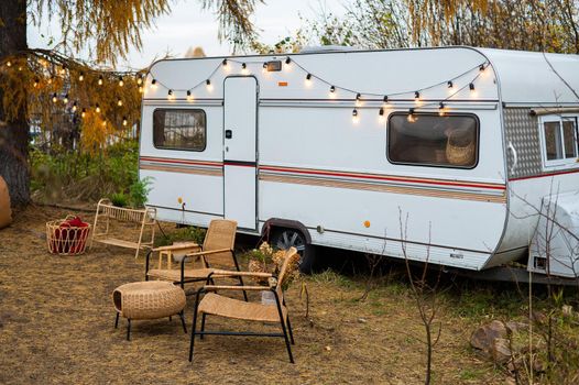 Camper or mobile home in the countryside. Cozy wicker furniture by a trailer in the autumn forest