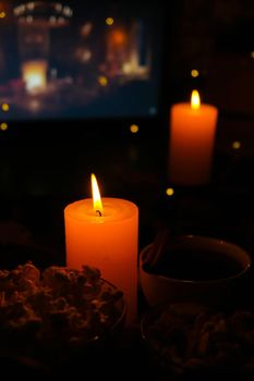 Movie on laptop at night in bedroom lit with candles. Pop corn. Autumn atmosphere at home. Cozy hygge style