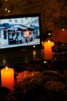 Movie on laptop at night in bedroom lit with candles. Pop corn. Autumn atmosphere at home. Cozy hygge style